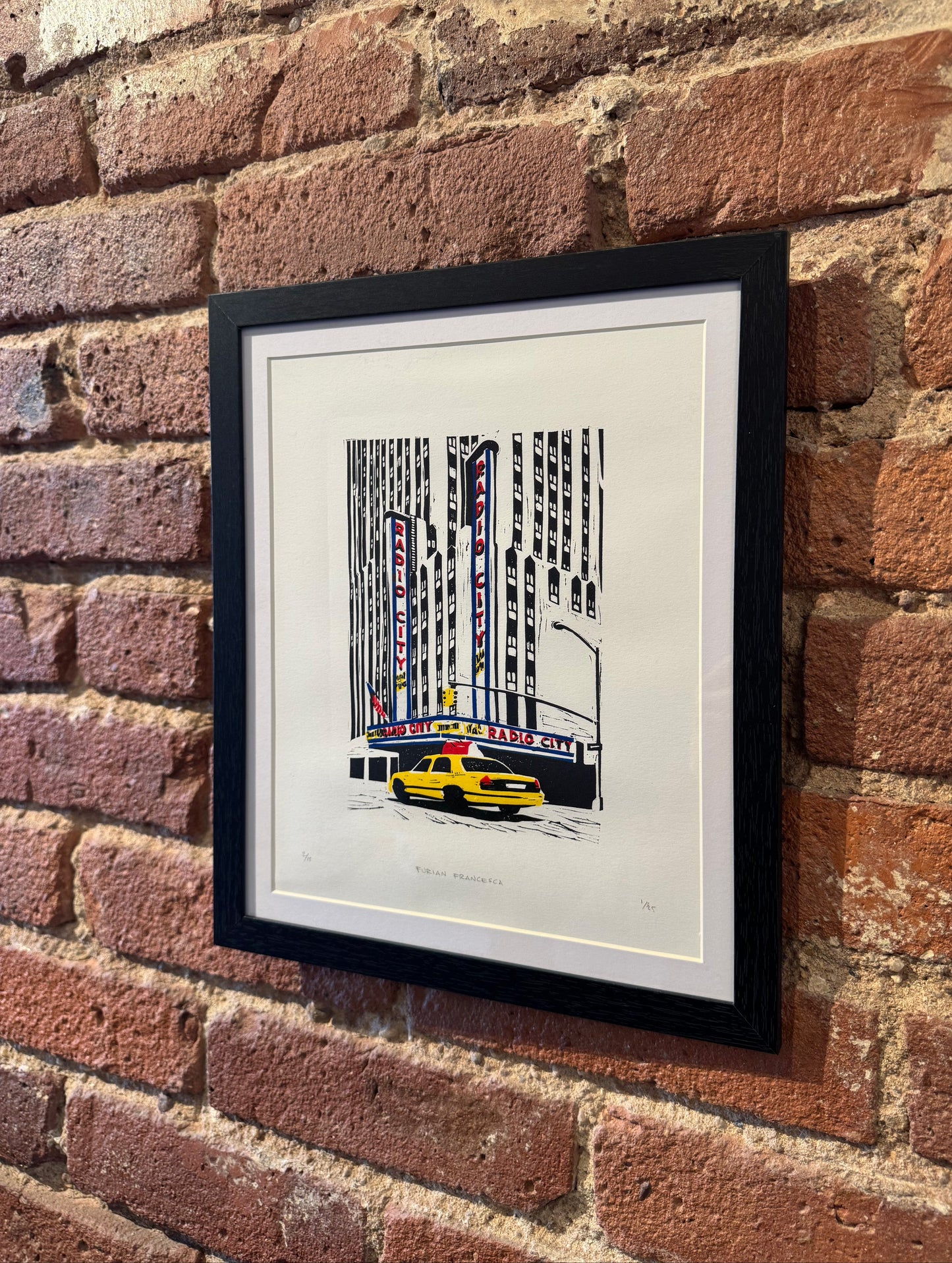 Framed artwork of a cityscape with a yellow taxi on a brick wall.